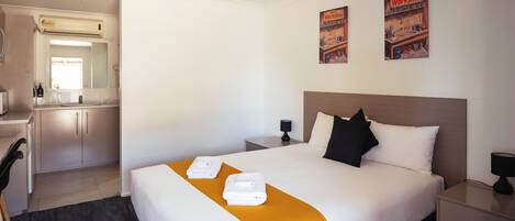 A hotel room with a bed, bedside tables, a desk, and an air conditioning unit.