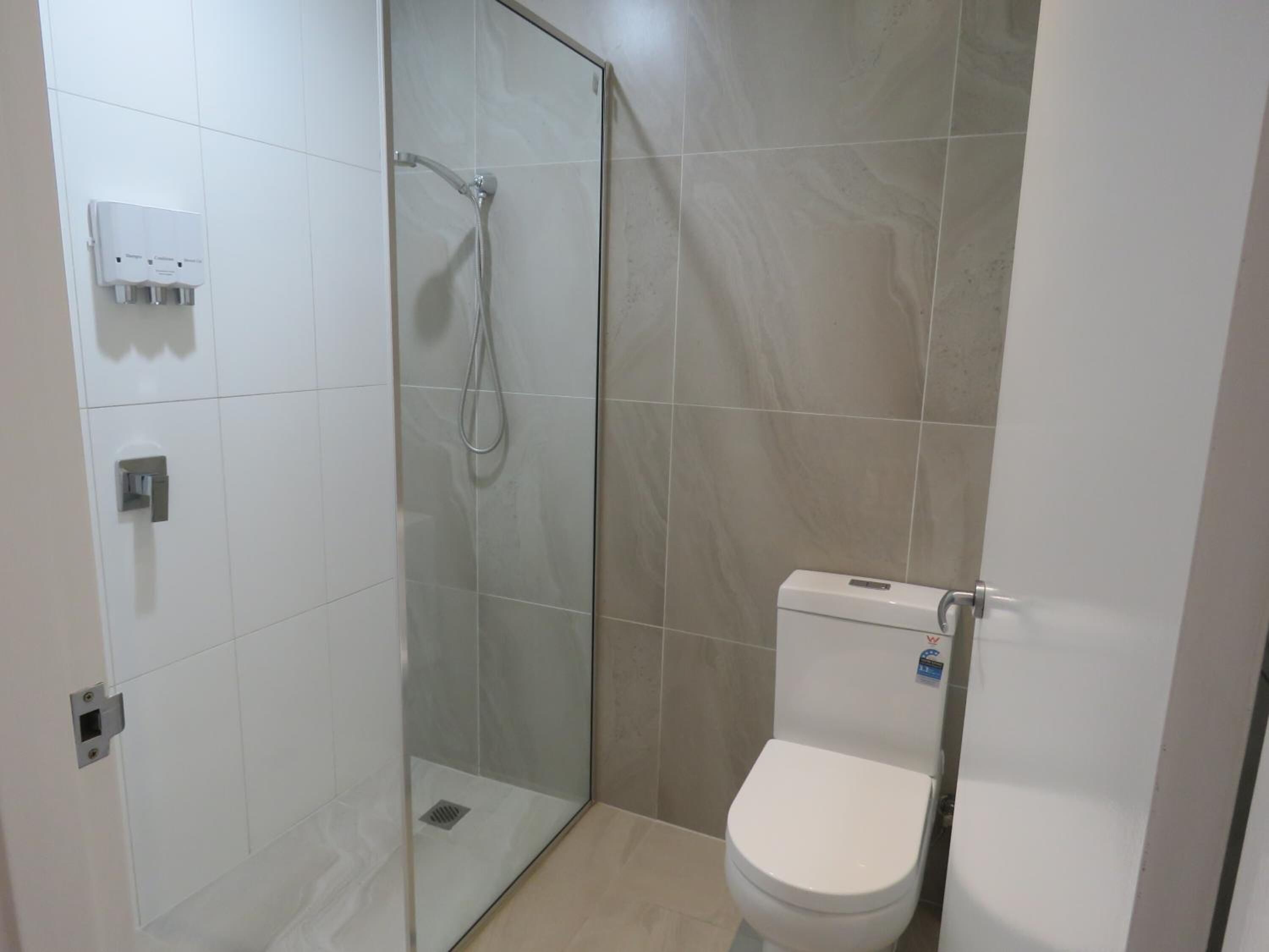 A modern bathroom with a glass-enclosed shower, a toilet, and a wall-mounted soap dispenser.