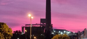 Ein großes Industriegebäude mit hohem Schornstein, Straßenlaternen und einem rosafarbenen Himmel.