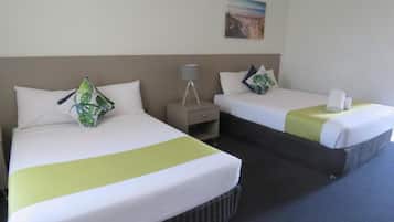 A hotel room with two beds, each with white bedding and green accents, a nightstand with a lamp, and a painting on the wall.