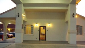 A hotel entrance with a covered driveway, two illuminated signs above the door, and a parking area with cars. - Winnquest Inn Near Ft. Sam Houston (San Antonio)