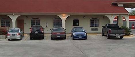 A building with a red roof and a parking lot with five cars parked in front.