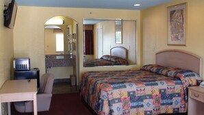 A hotel room with a bed, a desk, a chair, a mirror, a television, and a bathroom with a sink and mirror. - Winnquest Inn Near Ft. Sam Houston (San Antonio)