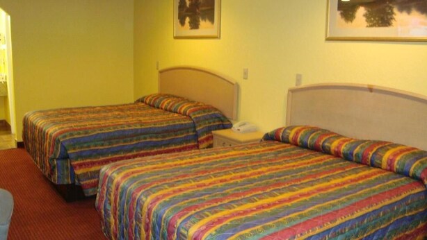A hotel room with two beds, each with a colorful striped bedspread. There is a nightstand with a phone and a lamp between the beds. - Winnquest Inn Near Ft. Sam Houston (San Antonio)