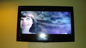 A television mounted on a wall displaying a blurred image of a person. - Winnquest Inn Near Ft. Sam Houston (San Antonio)