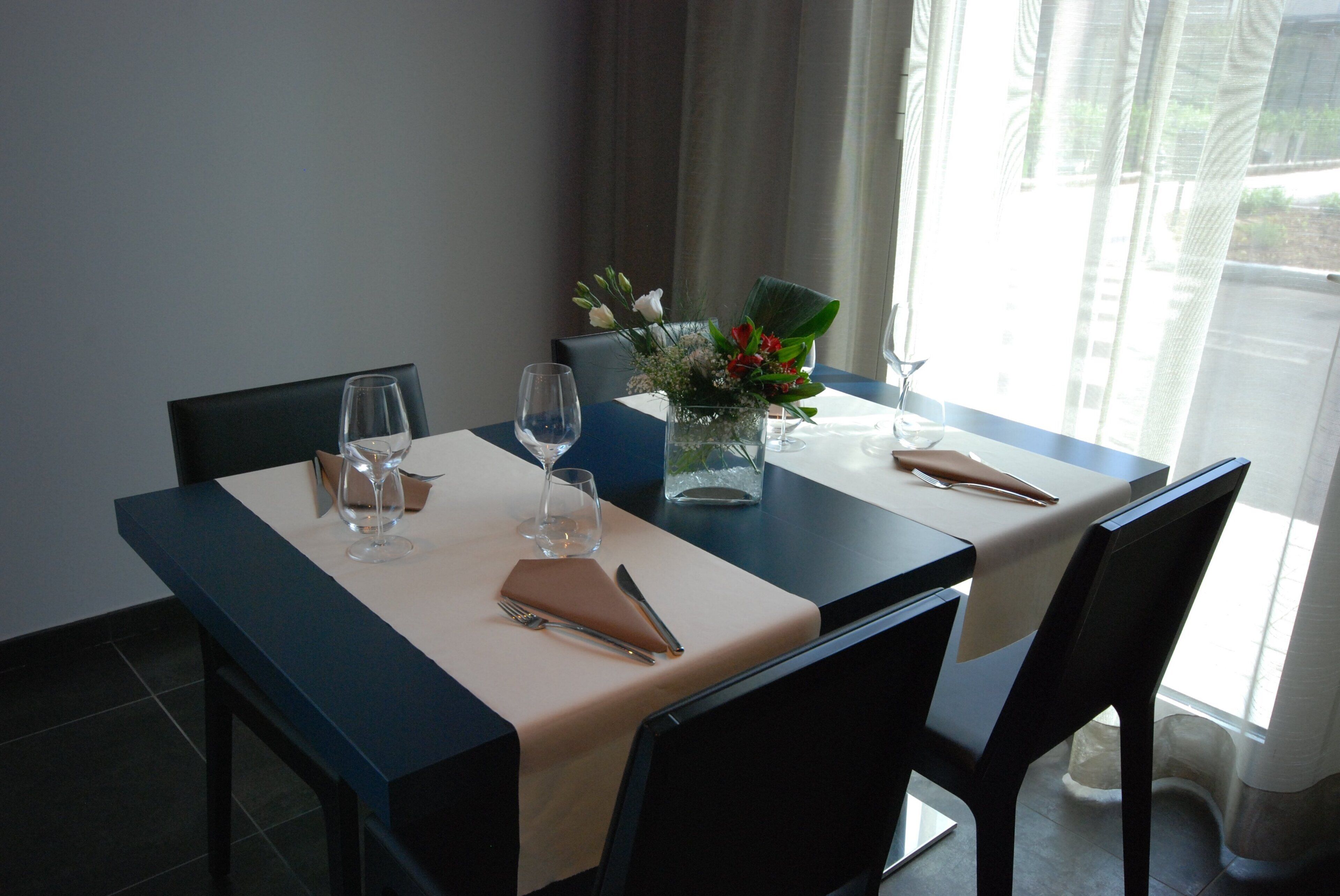 A dining table set with a vase of flowers, wine glasses, and cutlery.