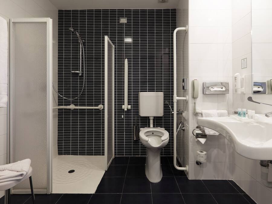 A modern bathroom with a shower, toilet, and sink, featuring black and white tiles and a white toilet paper holder.