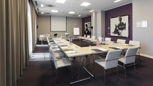 A conference room with a long table, chairs, a projector screen, and a poster on the wall. - Holiday Inn Milan Nord Zara by IHG (Cinisello Balsamo)