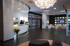 A modern reception area with a reception desk, a chandelier, and a seating area with sofas.