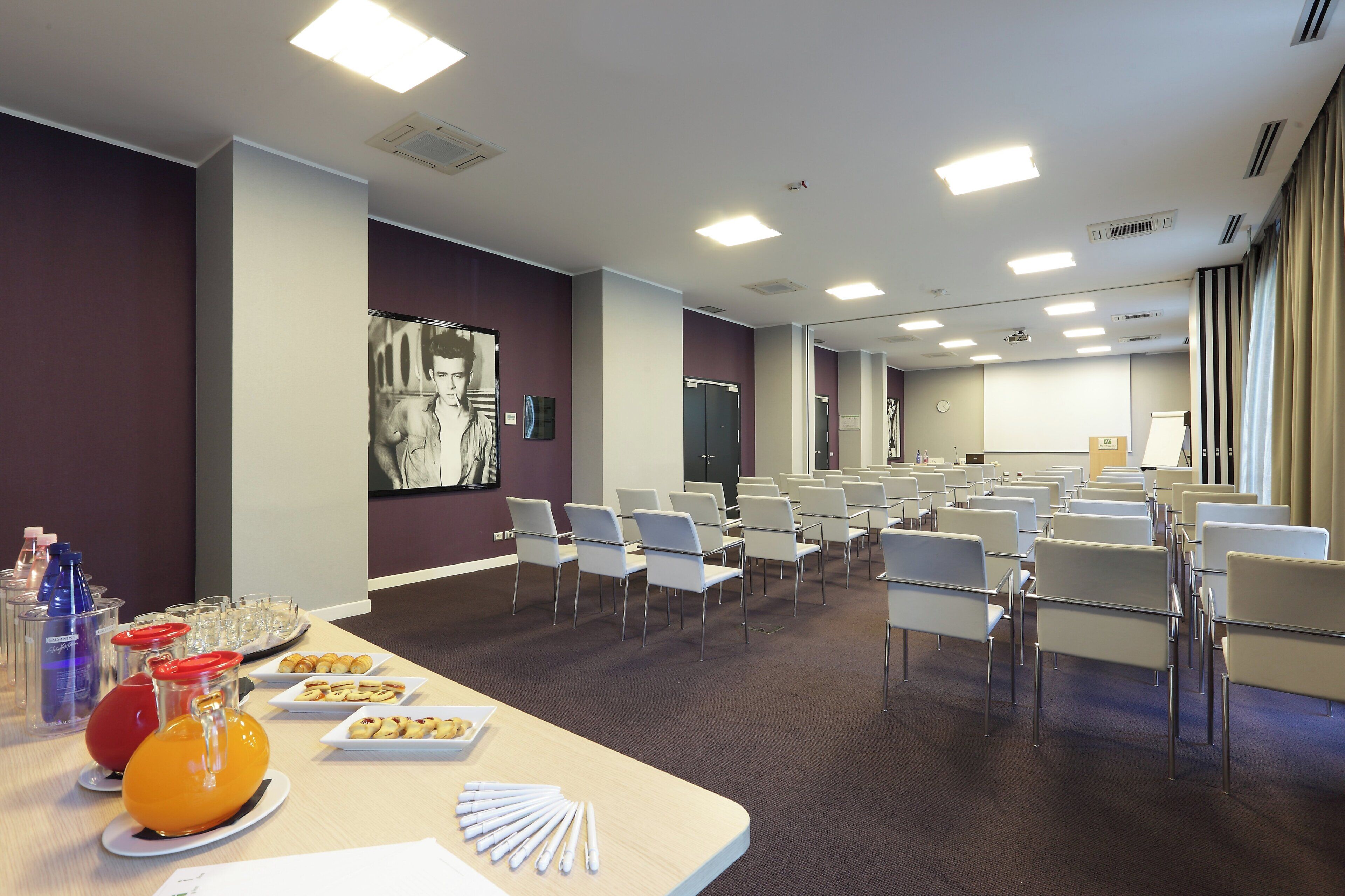 A conference room with rows of chairs, a presentation screen, and a buffet table with pastries and drinks.