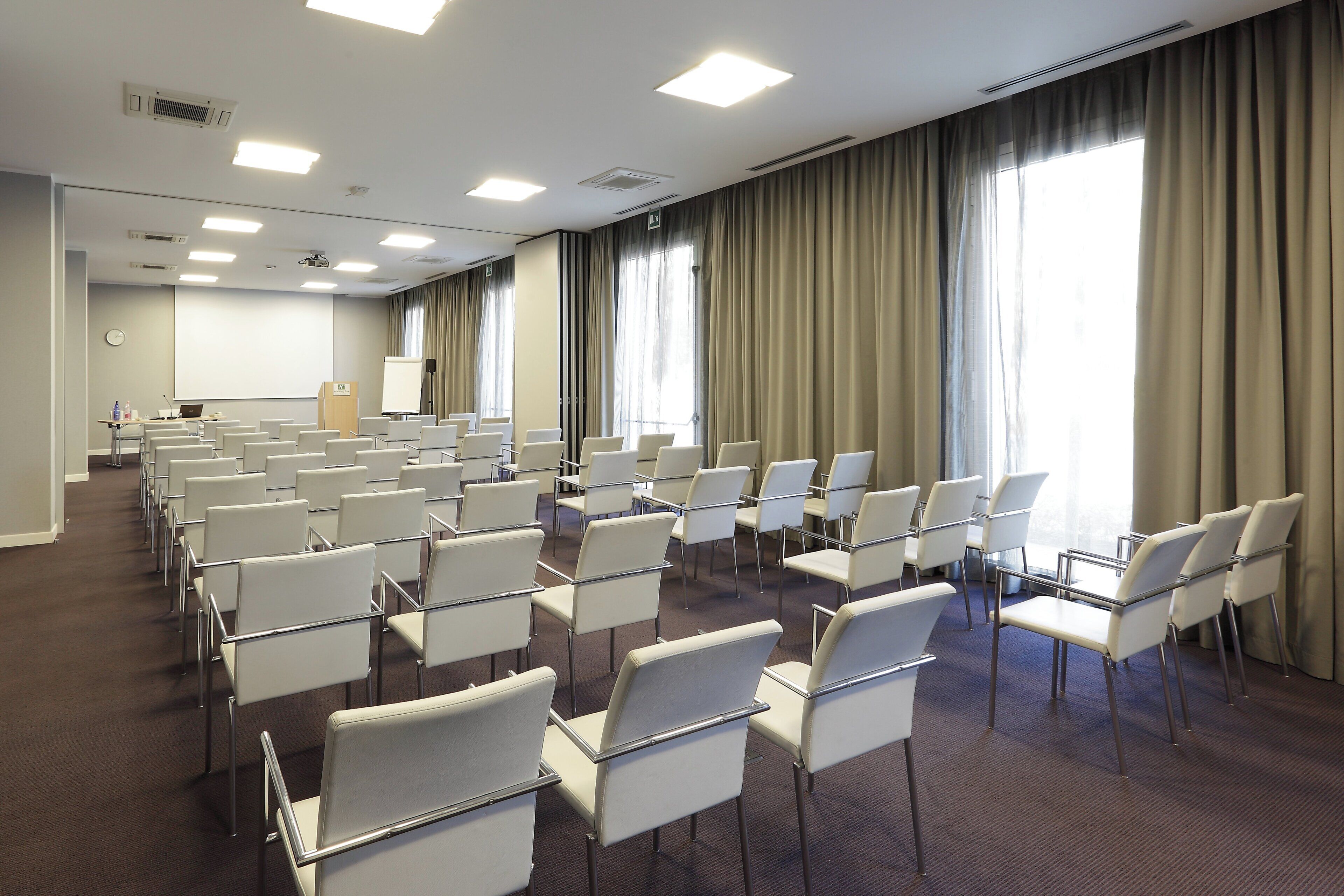 A conference room with rows of white chairs, a projector screen, and a podium.