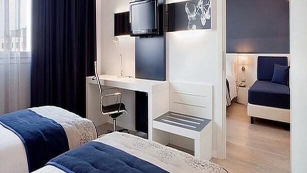 A modern hotel room with two beds, a desk with a chair, a flat-screen TV mounted on the wall, and a large window with curtains. - Holiday Inn Milan Nord Zara by IHG (Cinisello Balsamo)