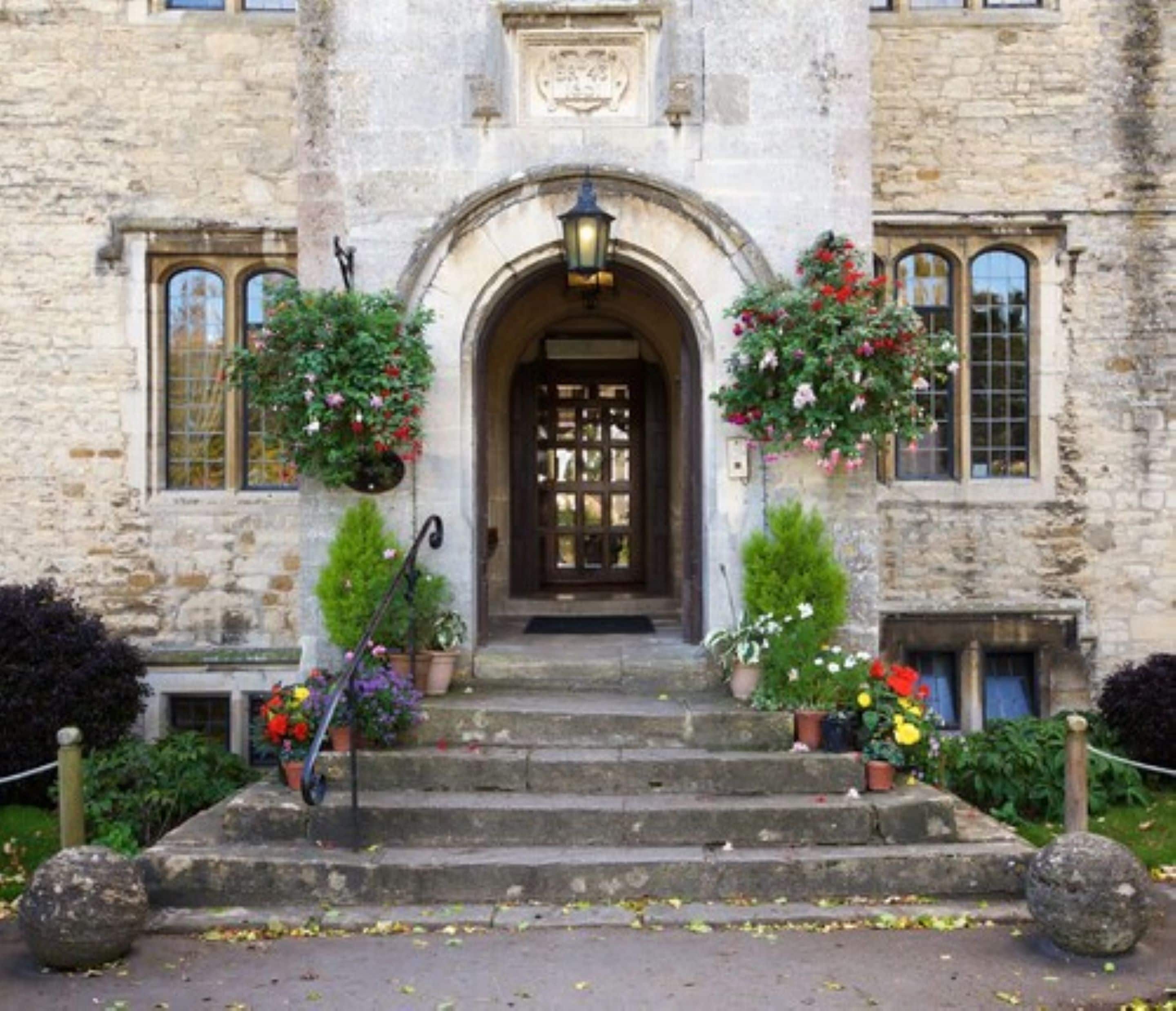 Un bâtiment en pierre avec une entrée centrale, flanqué de jardinières et d’un escalier menant à la porte.