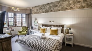 A hotel room with a large bed, a desk, a chair, a lamp, and a view of the outdoors through the window. - Stonehouse Court Hotel (Stonehouse)