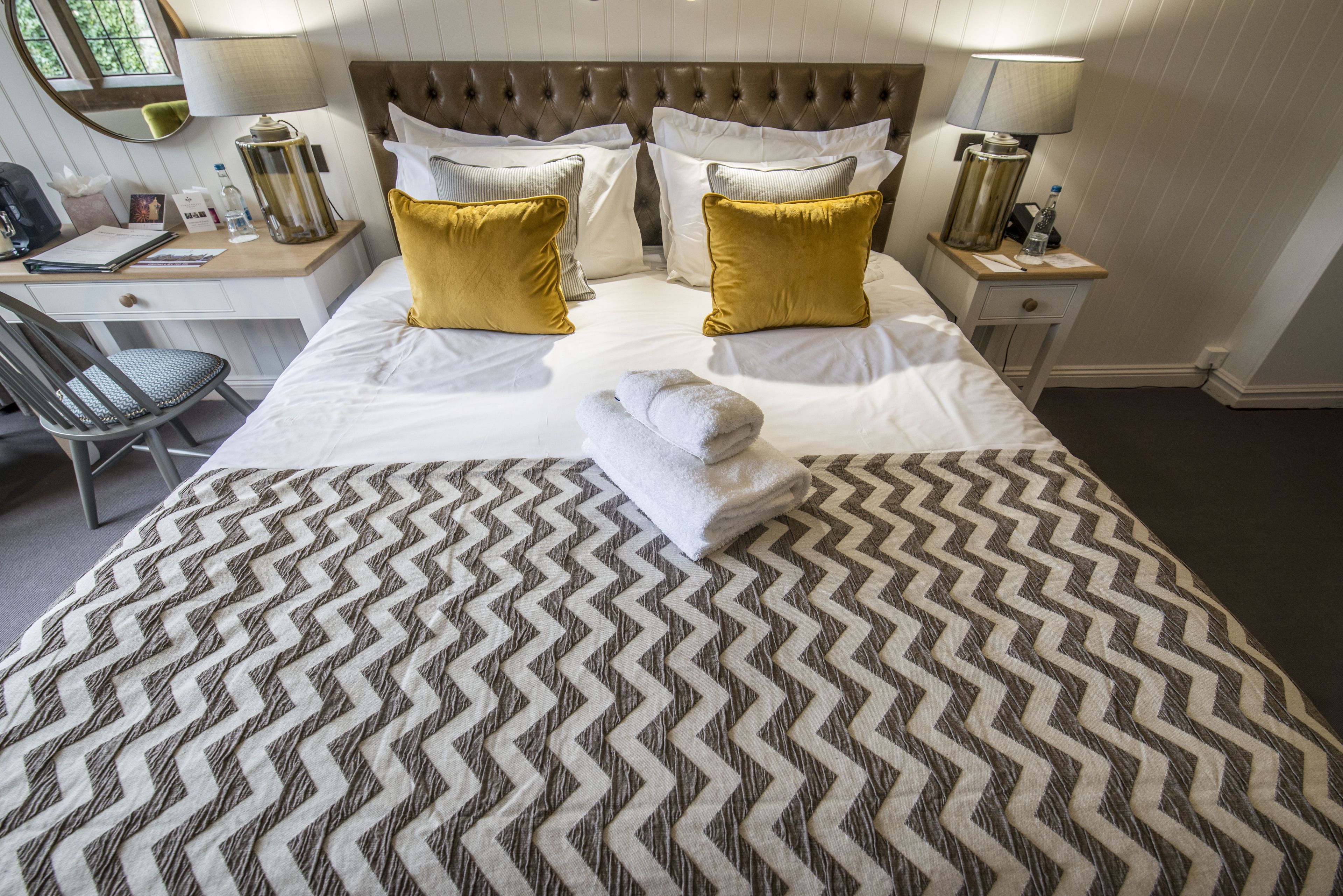 A neatly made bed with a patterned bedspread, two pillows, and a folded towel.