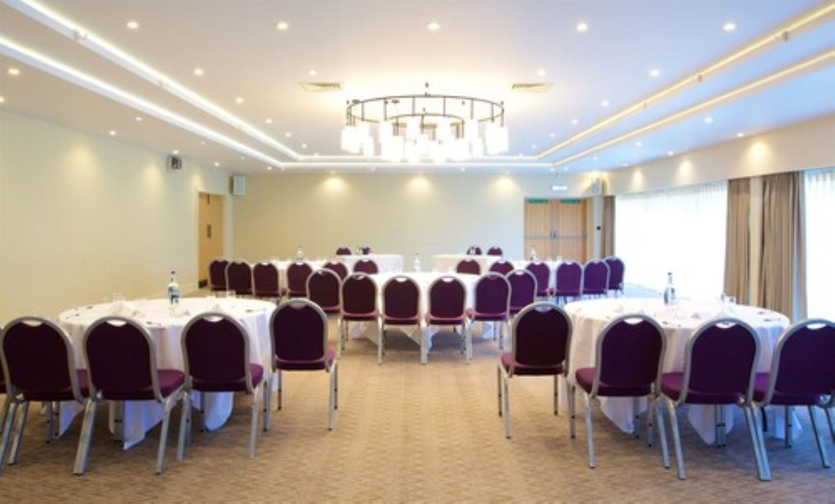 A conference room with round tables and chairs, a chandelier, and carpeted flooring.