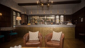 A bar area with leather chairs, a wooden table with a newspaper, and a bar stocked with bottles. - Stonehouse Court Hotel (Stonehouse)