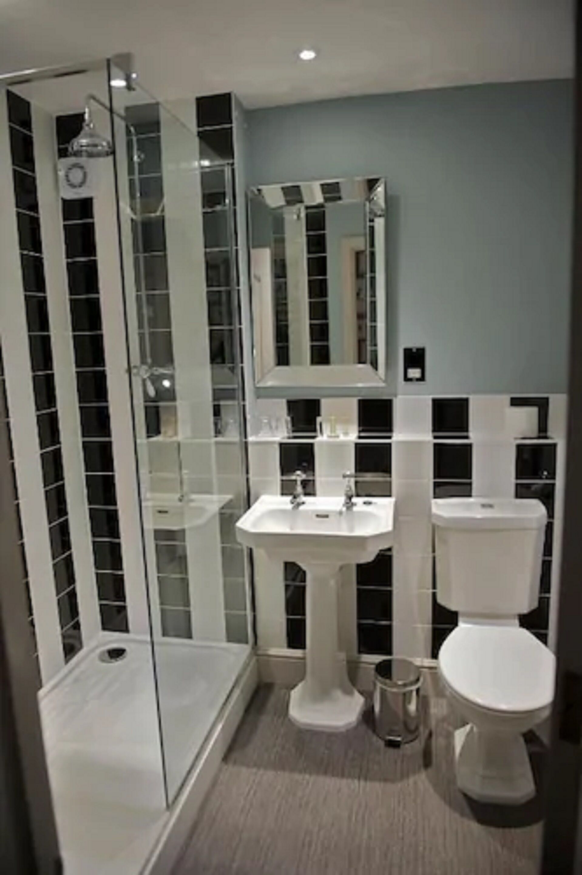 A bathroom with a glass shower enclosure, a pedestal sink, and a toilet.