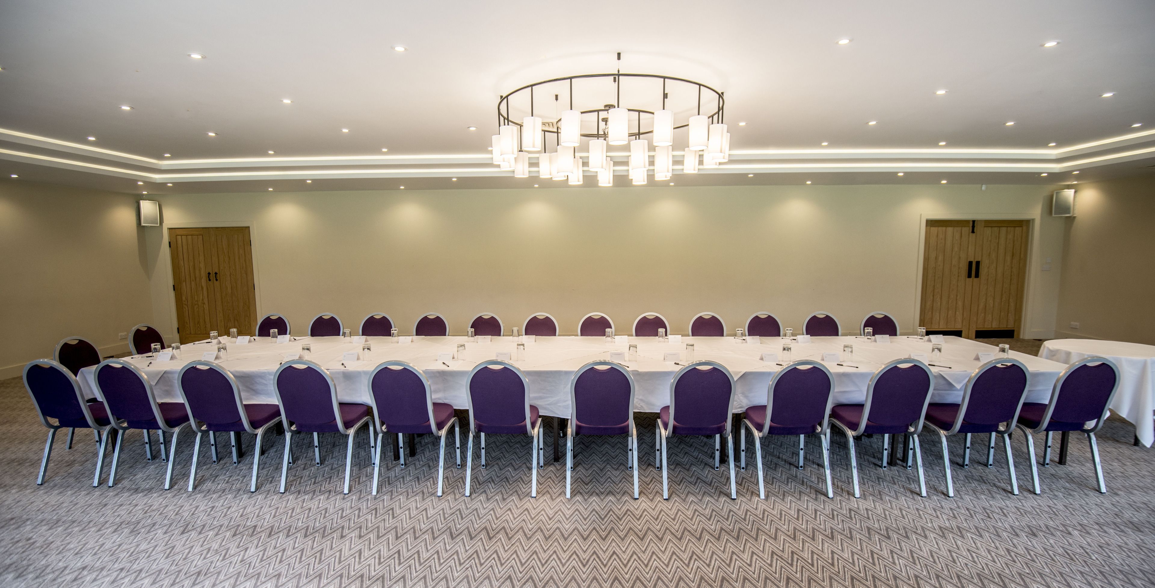 Ein Konferenzraum mit langem Tisch, violetten Stühlen und einer modernen Pendelleuchte.