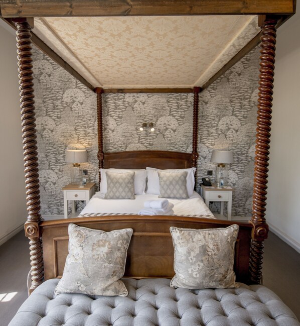 A four-poster bed with a tufted headboard, two nightstands with lamps, and a floral-patterned wallpaper. - Stonehouse Court Hotel (Stonehouse)