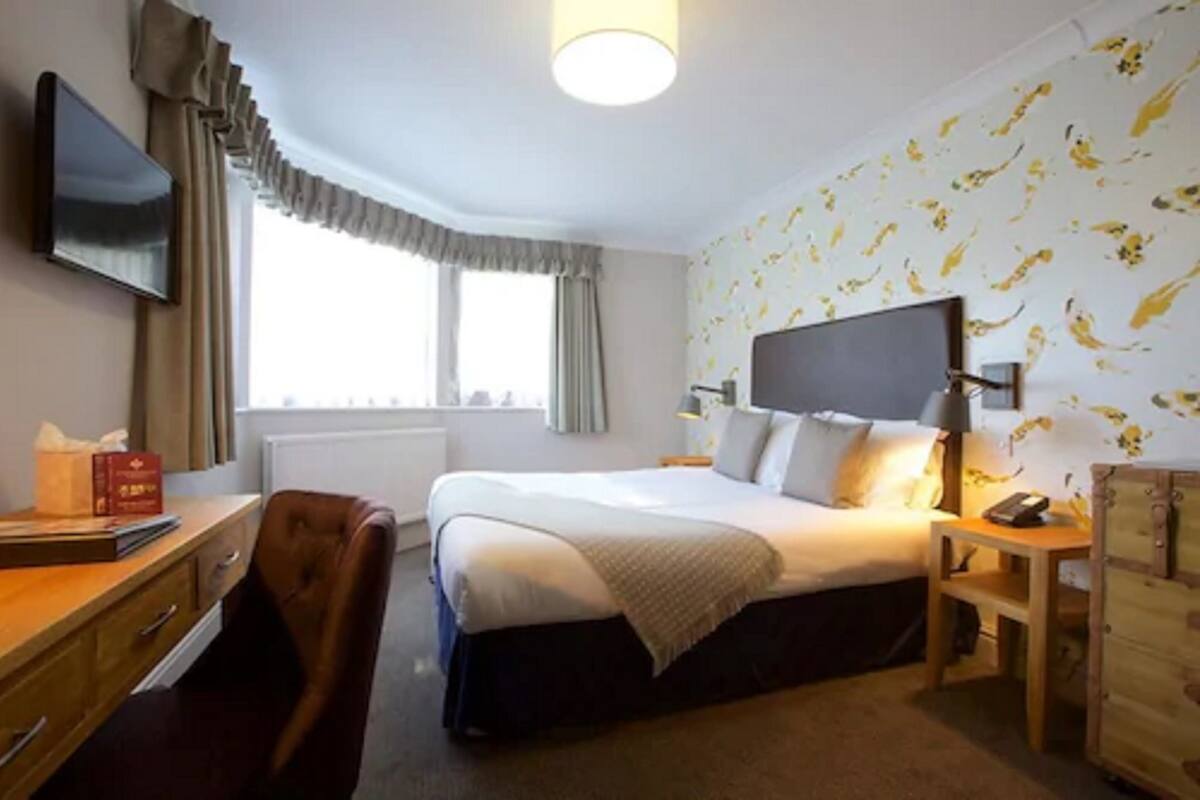 A hotel room with a bed, a desk, a chair, a TV, and a window with curtains.