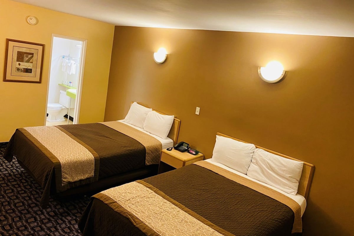 Ett hotellrum med två sängar, ett nattduksbord med en telefon och ett badrum som syns genom en öppen dörr.