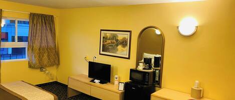 A hotel room with a bed, a desk, a chair, a television, a coffee maker, a mirror, and a window with curtains.
