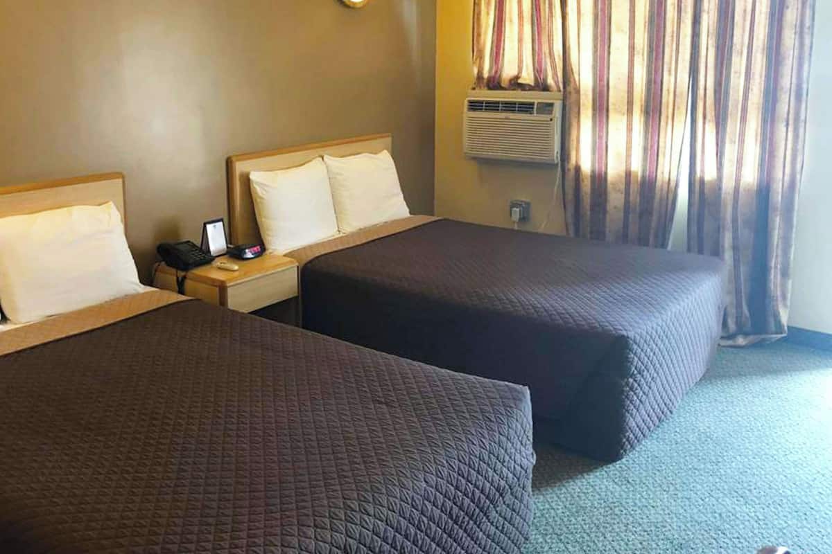 Ett hotellrum med två sängar, ett nattduksbord med en telefon och en lampa samt ett fönster med gardiner.
