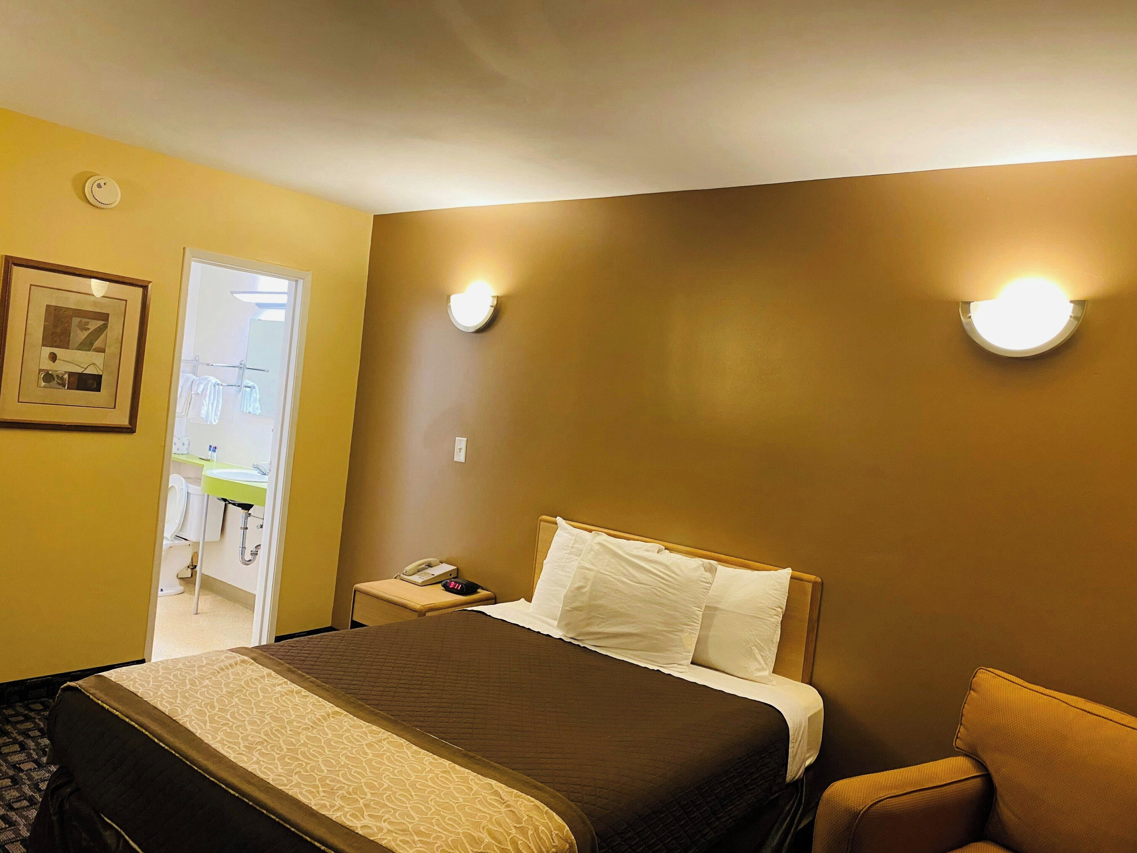 Habitación de hotel con cama, mesita de noche, lámpara y puerta que da al baño.