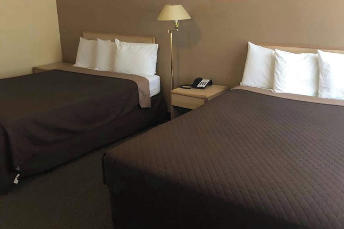 A hotel room with two beds, a bedside table with a lamp, and a phone.