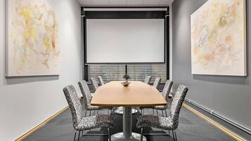 Un salón de conferencias con una gran mesa y sillas estampadas, rodeado de arte abstracto en las paredes.