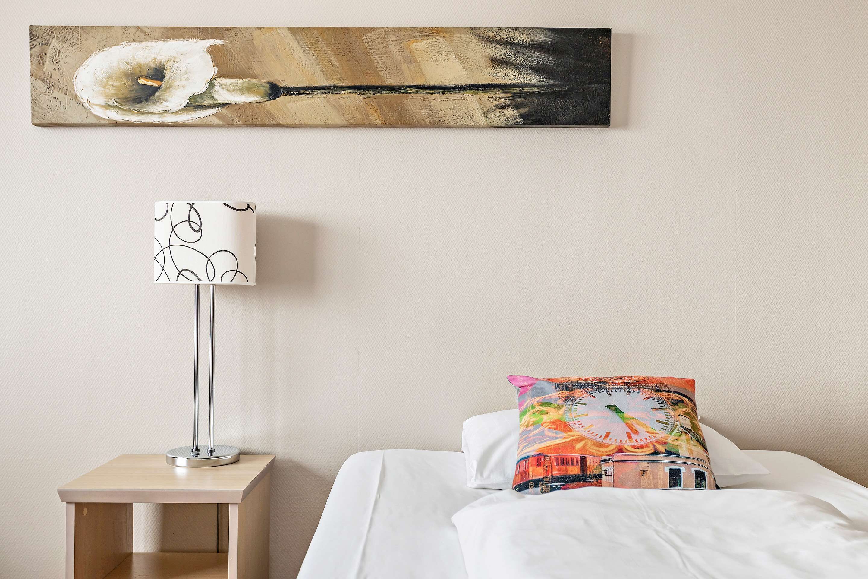 Una habitación de hotel con una cama, una mesita de noche con lámpara y un cuadro colgado en la pared.