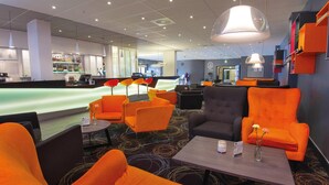 Un moderno vestíbulo de hotel con asientos naranja, una zona de bar y un mostrador de recepción.