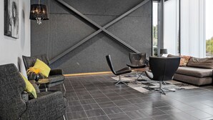 Un interior moderno con una pared texturizada oscura, un techo con estructura en forma de cruz y una variedad de asientos, incluyendo un sofá y sillas.