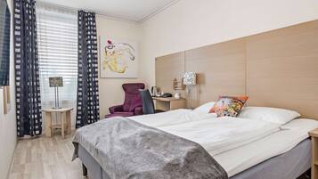 A hotel room with a bed, a desk, a chair, a lamp, and a painting on the wall.