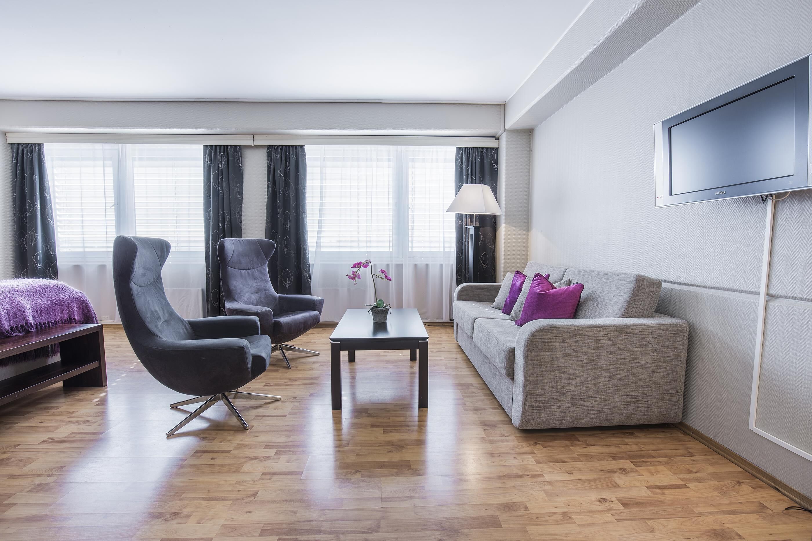 En moderne stue med sofa, to lænestole, sofabord og fjernsyn monteret på væggen.