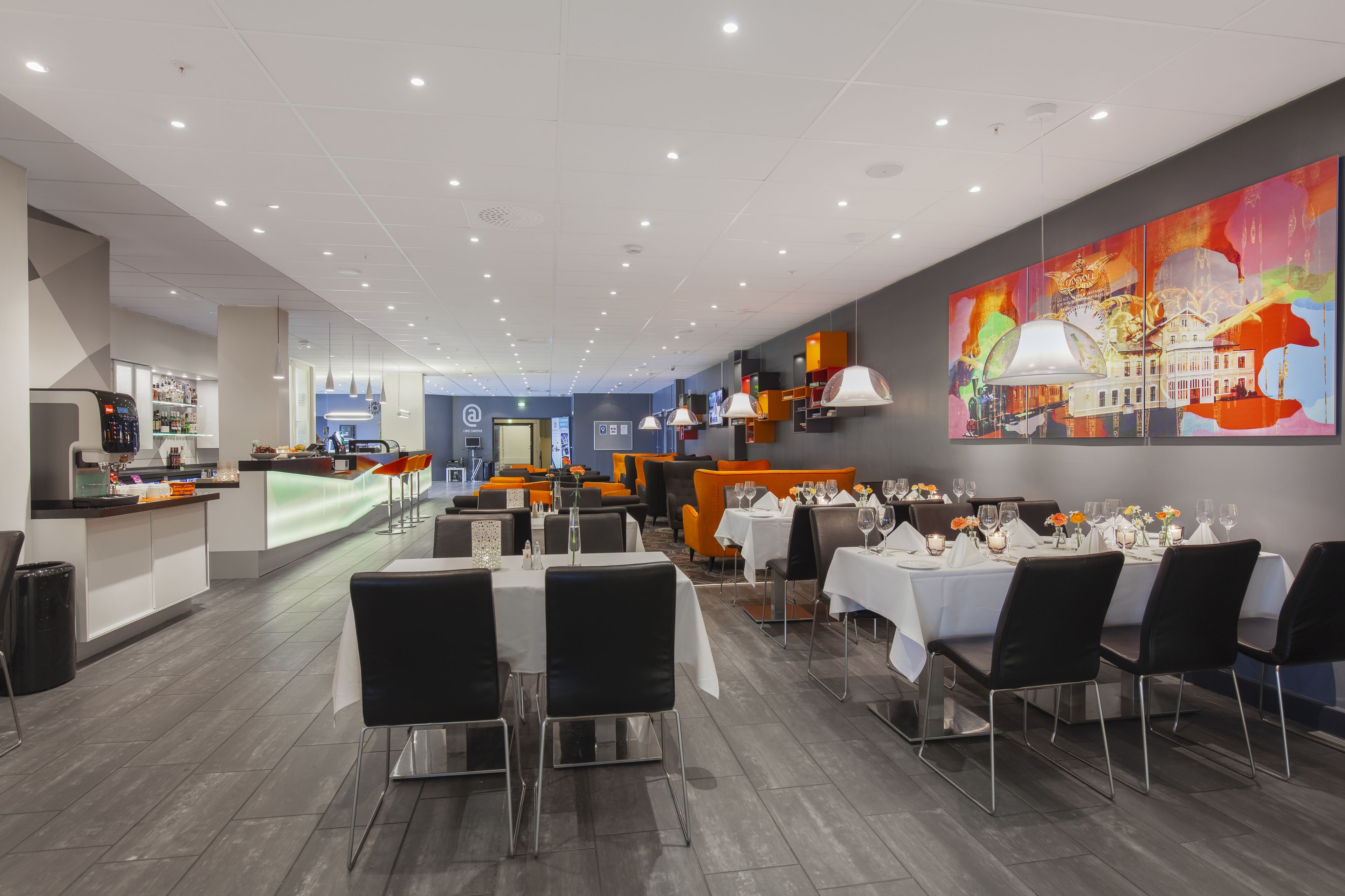 A modern restaurant with a long counter, multiple dining tables, and a colorful abstract painting on the wall.