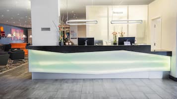 Zona de recepción de hotel con un diseño moderno, que incluye un mostrador de recepción, dos monitores de computadora y un letrero que dice 'Resepsjon'.