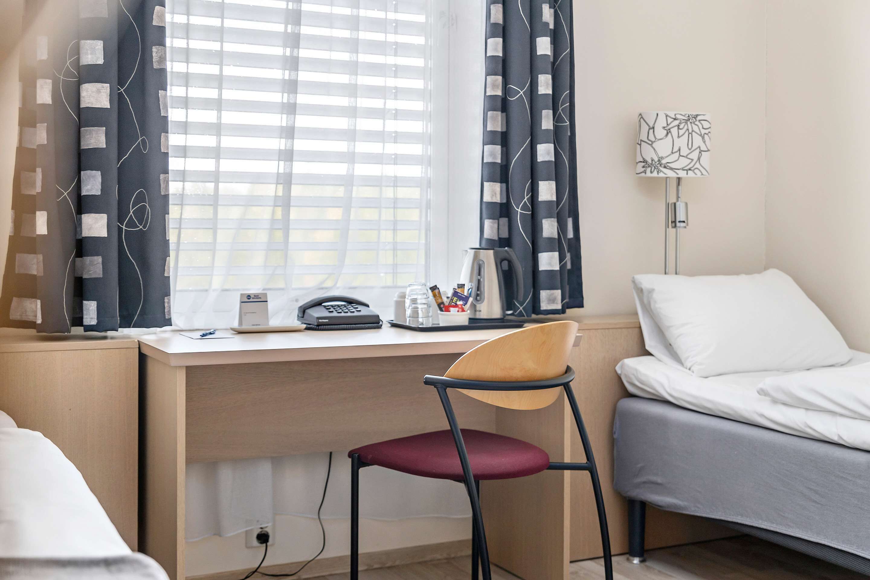 A hotel room with a desk, a chair, a bed, and a window with curtains.