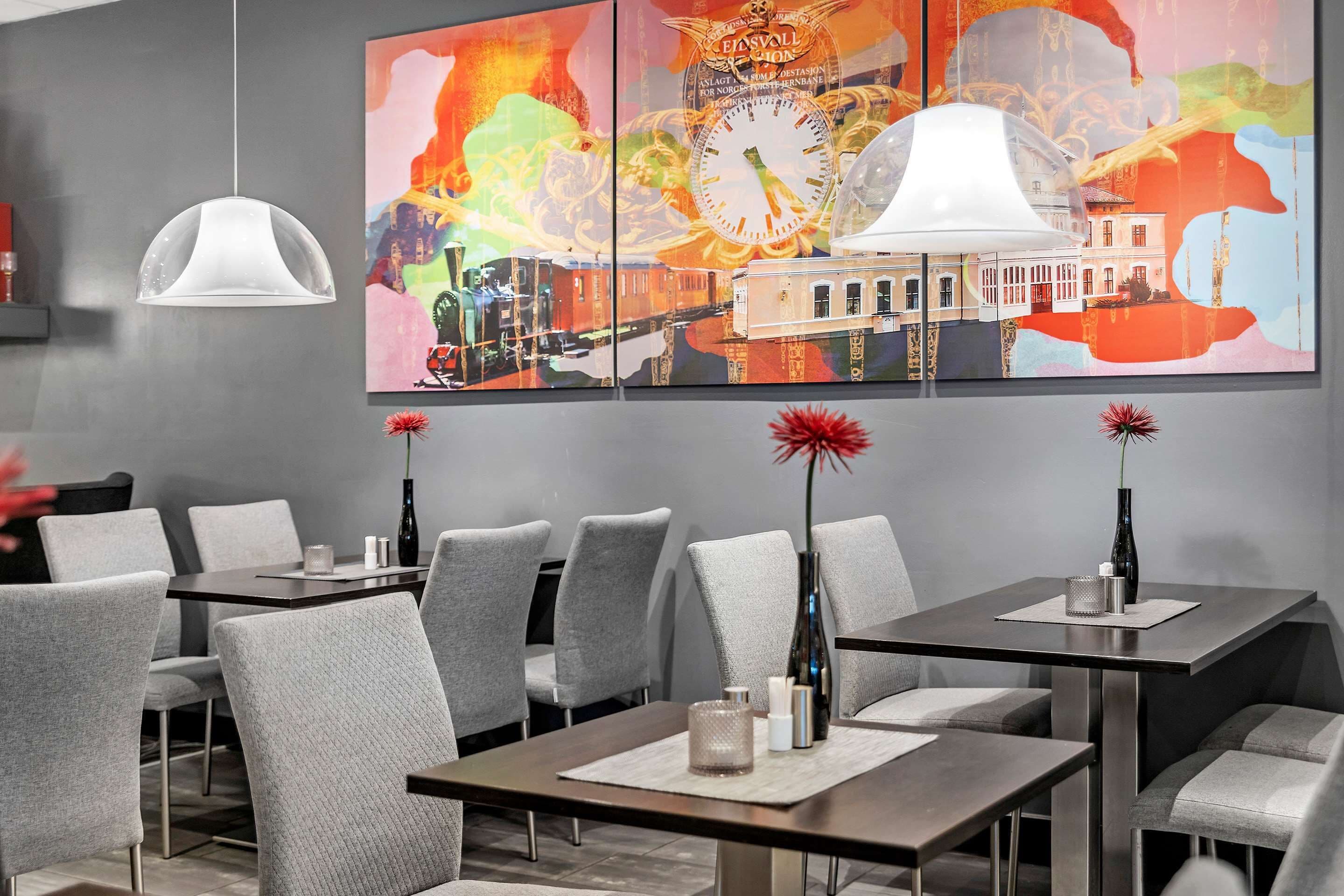 A modern dining area with grey upholstered chairs, a central table with a vase and candles, and a colorful abstract painting above.