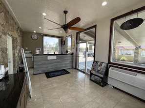 A reception area with a stone wall, a wooden reception desk, a ceiling fan, and a view of the parking lot through glass doors. - Motel 6 Hermison, OR - Umatila (Hermiston)