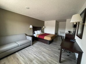 A hotel room with a bed, a sofa, a desk, and a lamp.