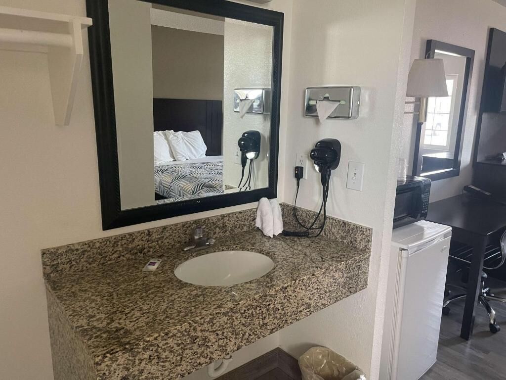 A hotel bathroom with a granite countertop sink, a mirror, a hairdryer, and a towel rack.