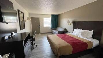 A hotel room with a bed, a desk, a chair, a television, and a window with curtains.