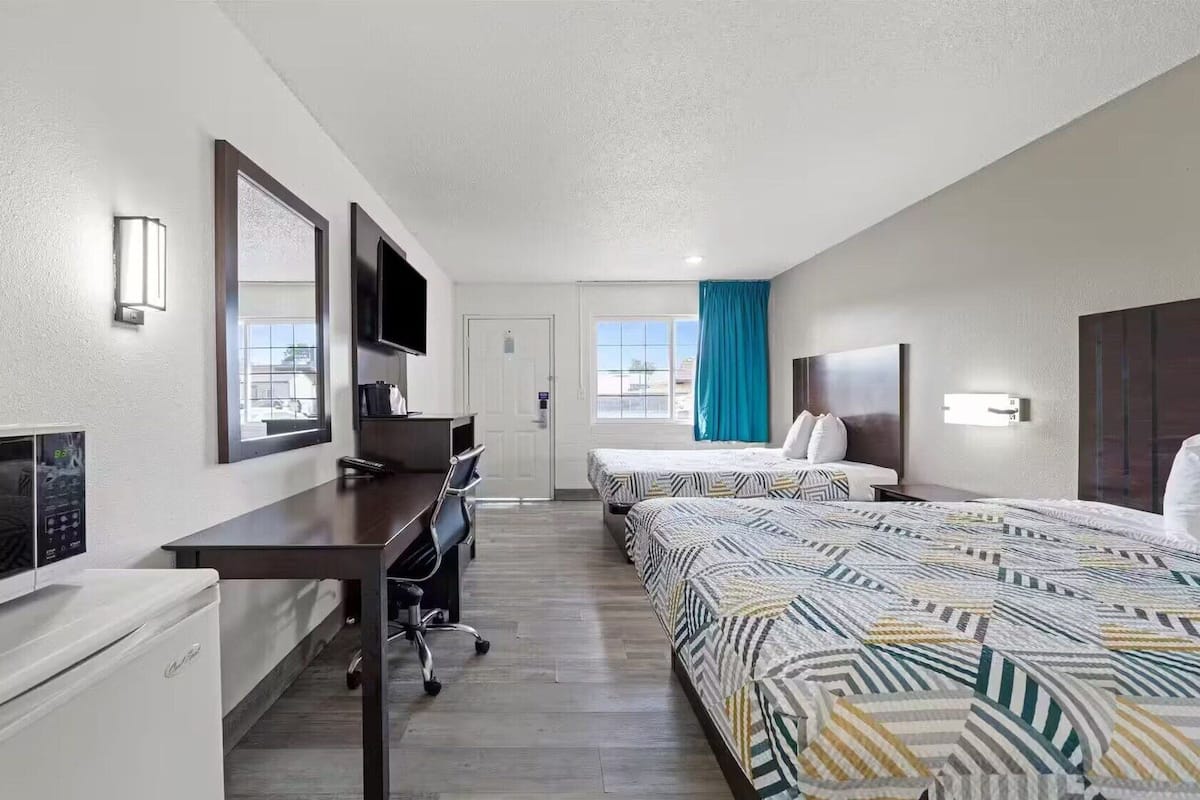Quarto de hotel com duas camas, uma escrivaninha, uma televisão e uma janela com vista.