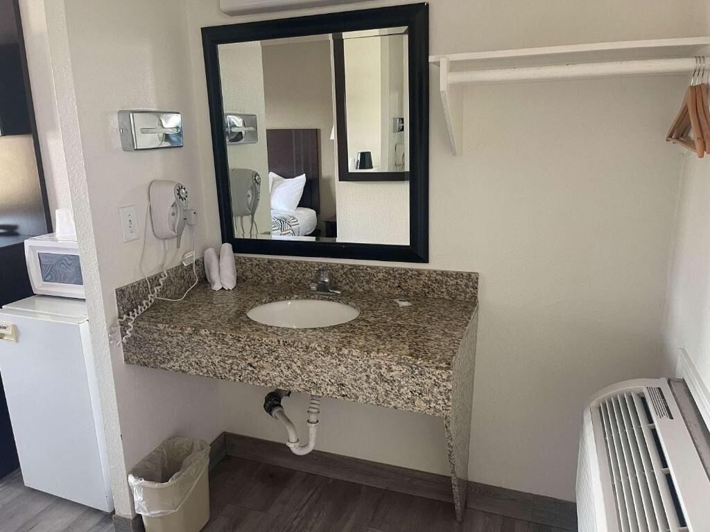A bathroom with a granite countertop sink, a mirror, a hairdryer, and a radiator.