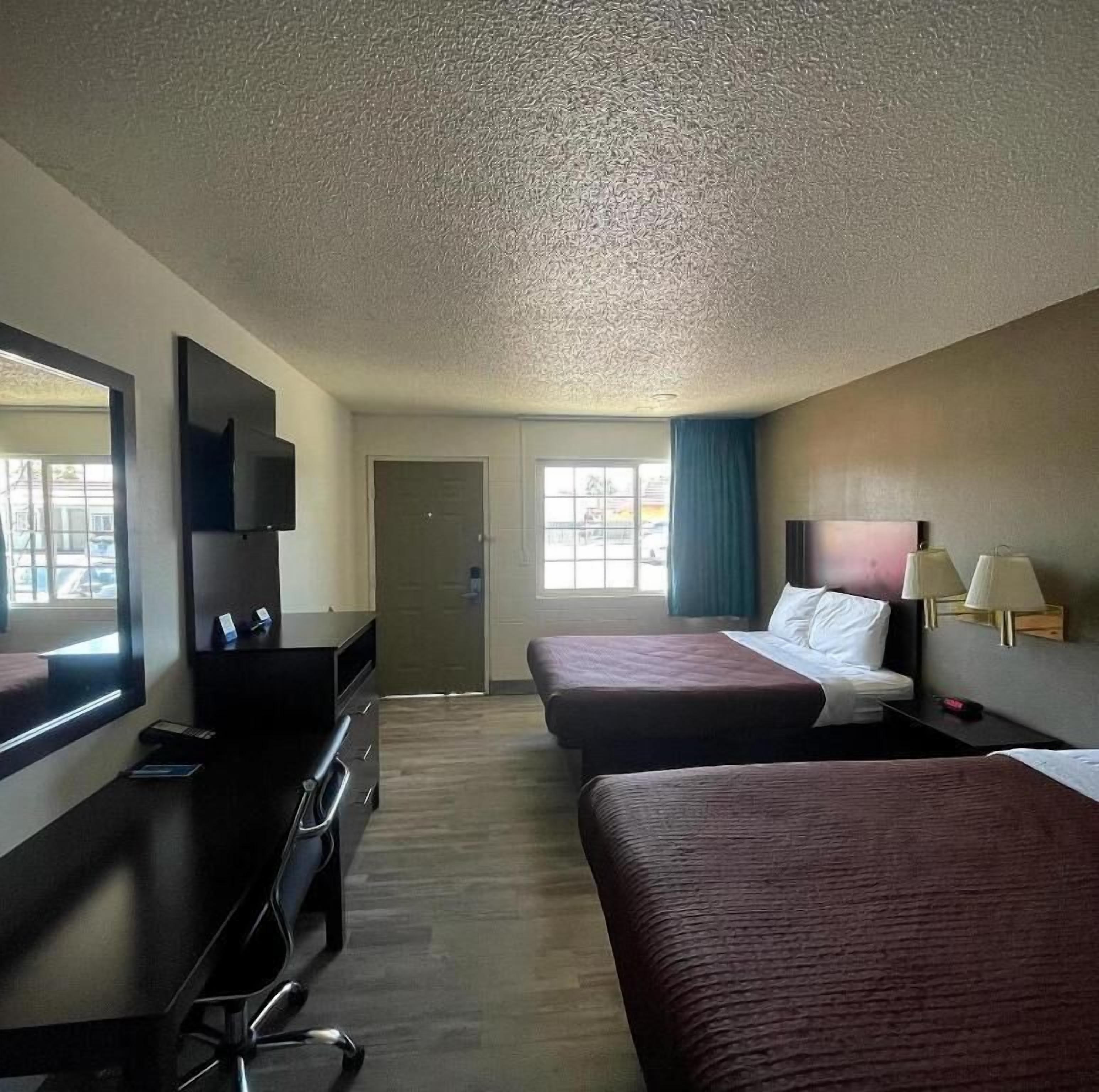 A hotel room with two beds, a desk with a chair, a television, and a window with curtains.