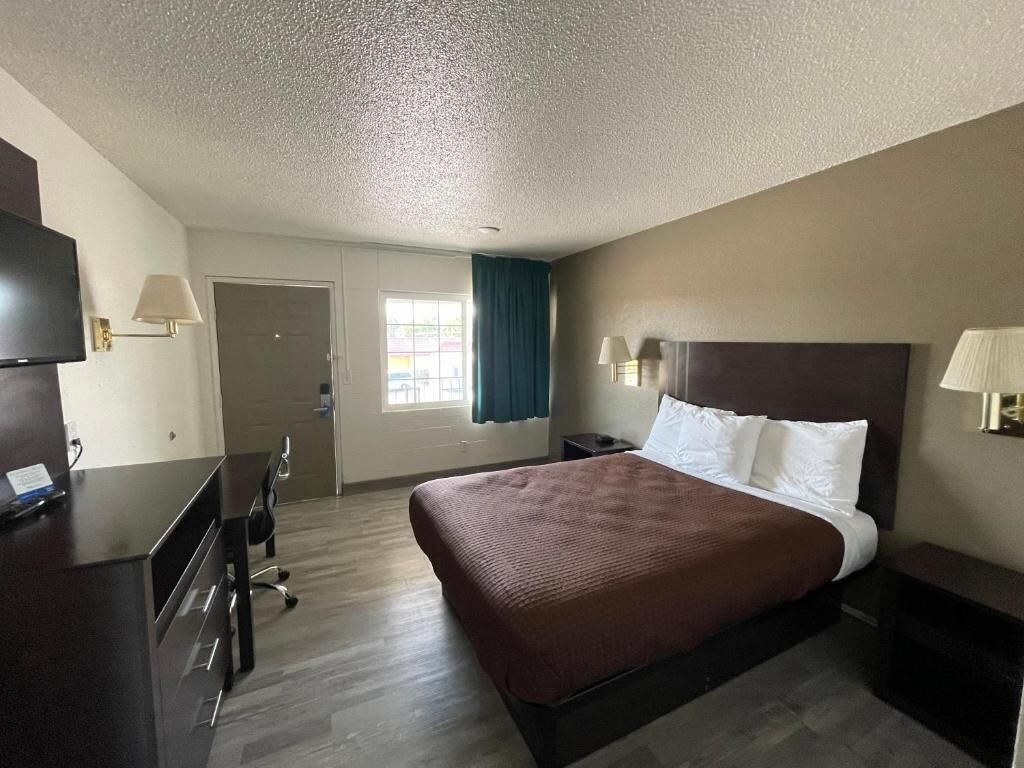 A hotel room with a bed, desk, chair, and a television.