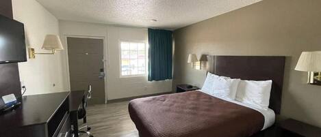 A hotel room with a bed, desk, chair, and a television.