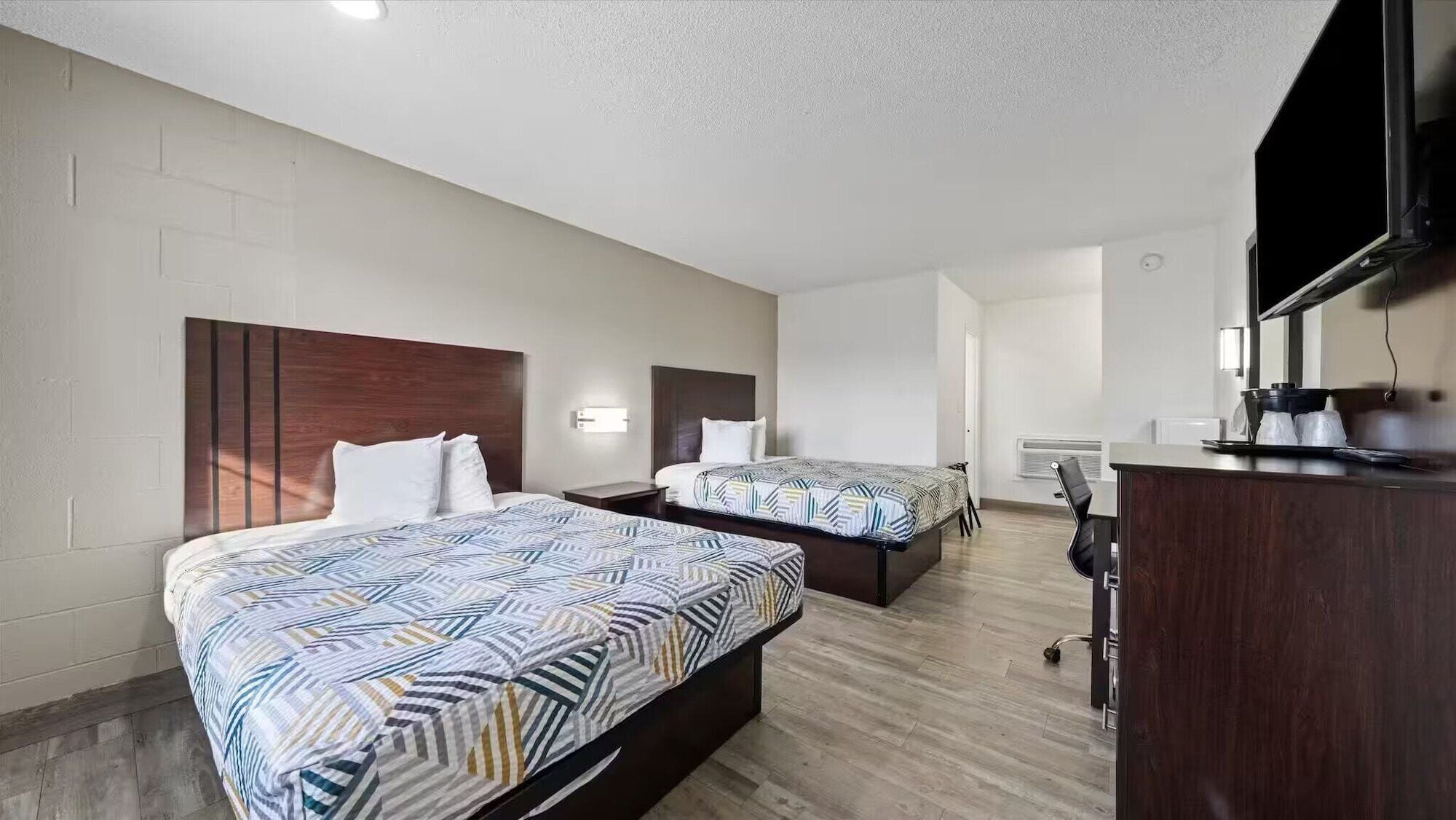 Ein Hotelzimmer mit zwei Betten, einem Schreibtisch, einem Fernseher und einer Klimaanlage.